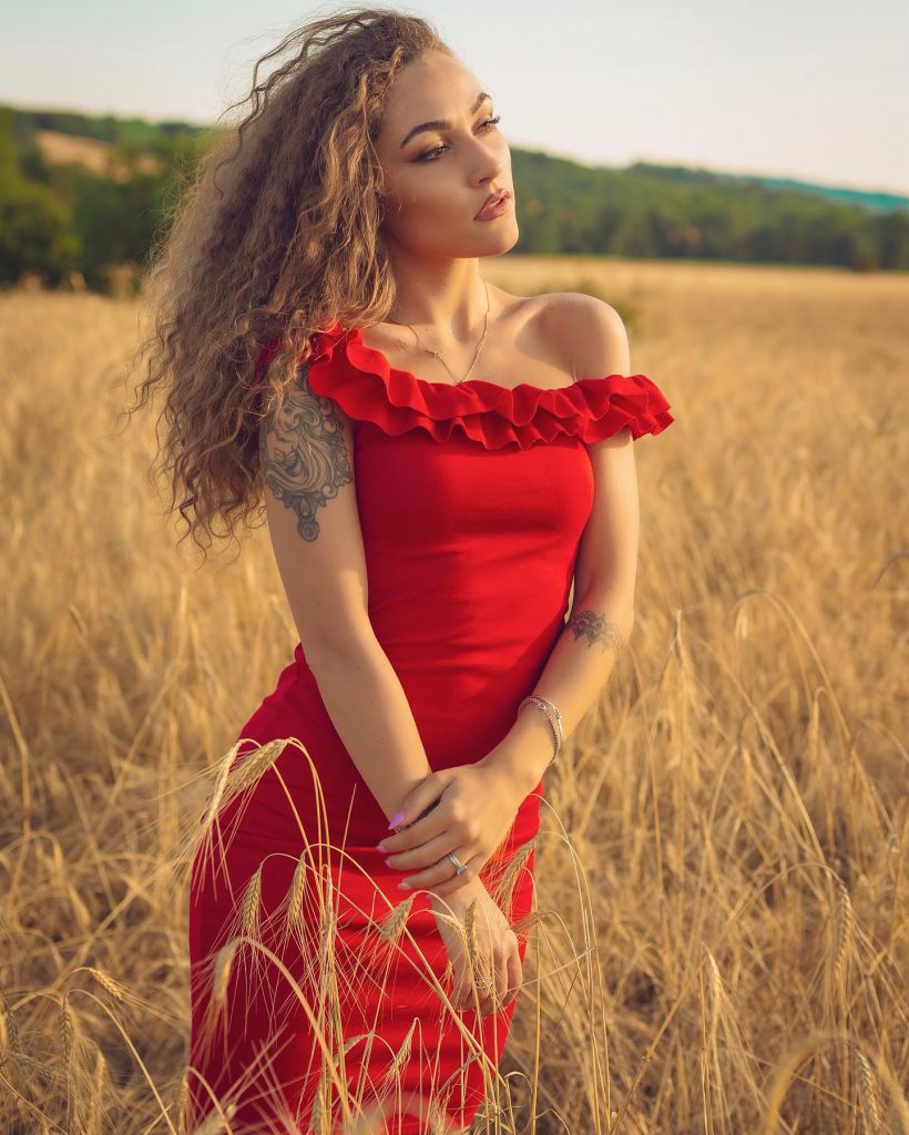 Carlotta in abito rosso in un campo di grano a Pienza Val d'Orcia